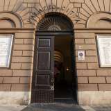 L�iscrizione in lettere di bronzo sormonta la lunetta del portone, la quale si apre nella fascia in bugnato color terra della struttura